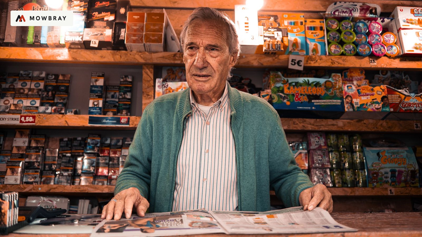 An older shopkeeper behind the counter of a crowded corner shop