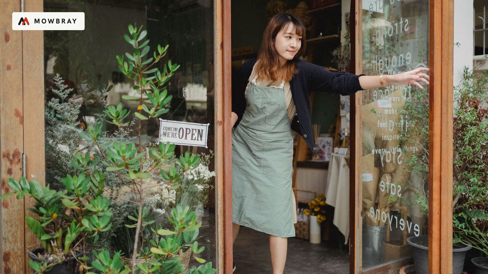 A shop owner opening the door of her plant-filled shop, an Open sign in the window