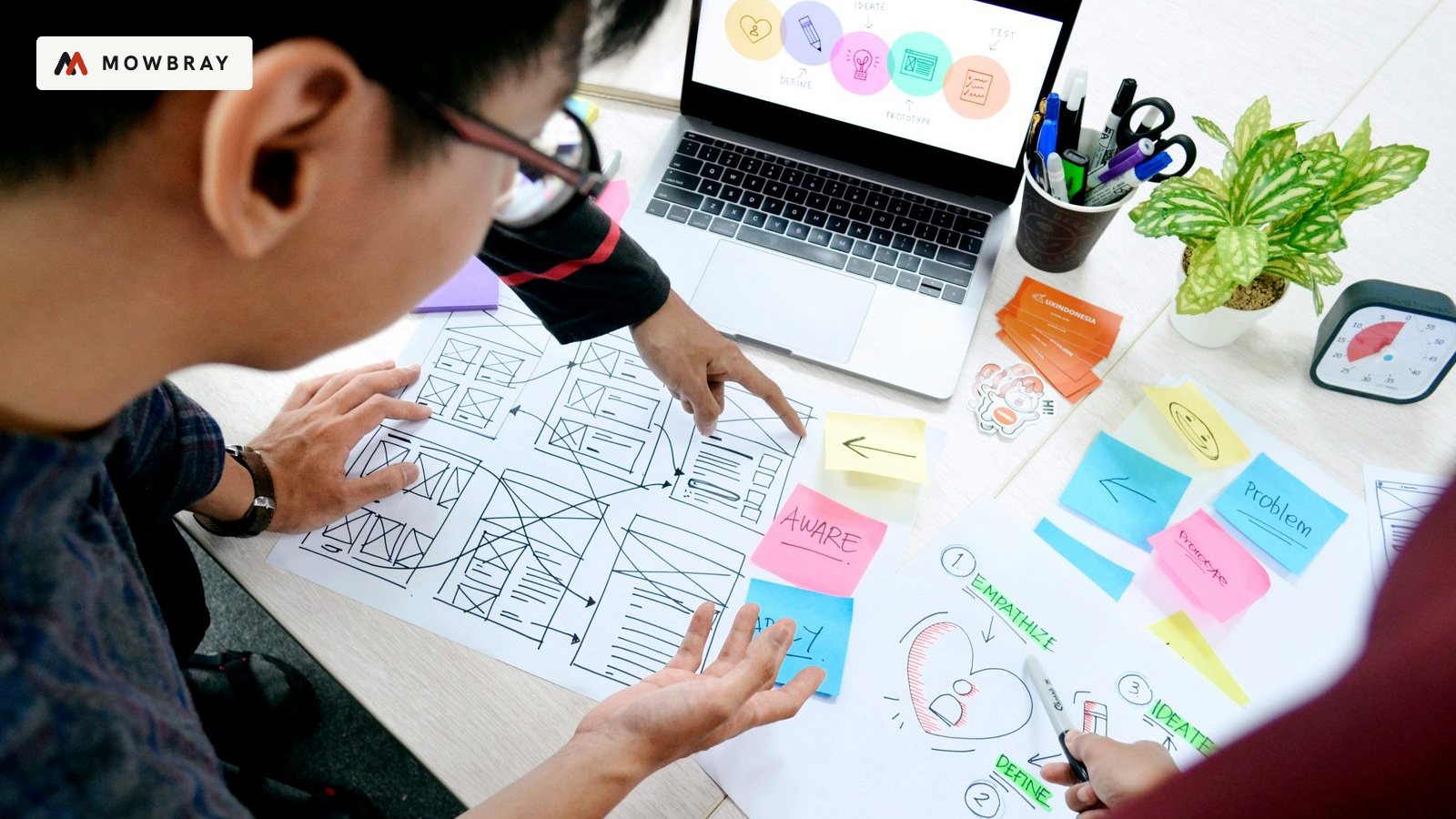 Two people planning on paper with sticky notes beside a laptop