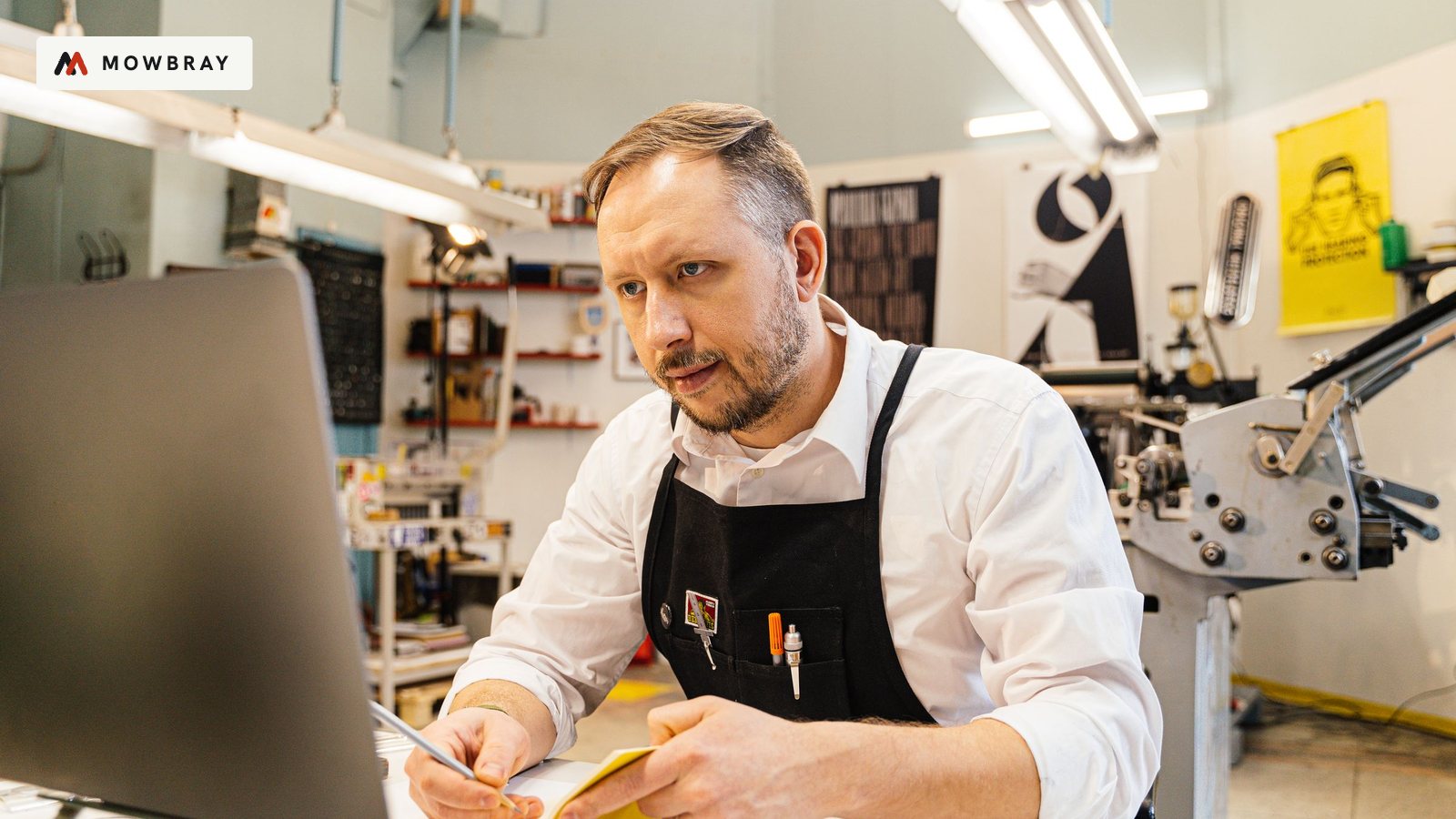 A craftsman in an apron working on a laptop in his workshop