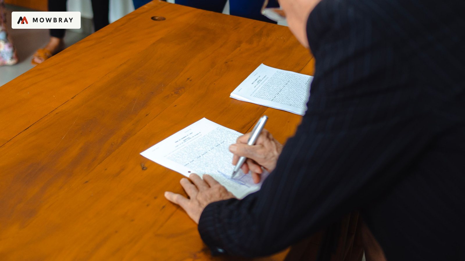 An older man in a suit signing a document at a wooden desk